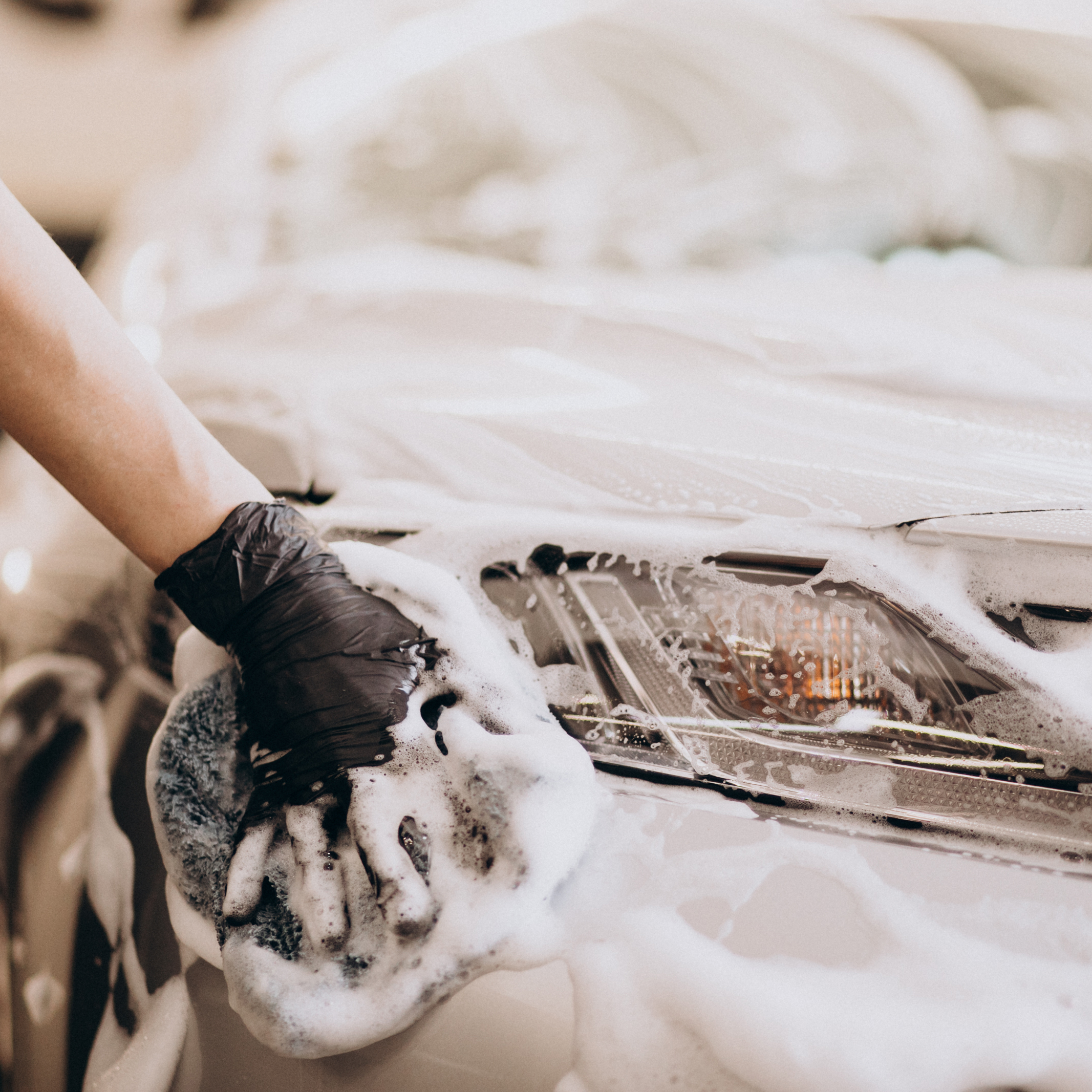 Auto detailing expert in the RGV hand washing a car covered in thick snow foam for a deep exterior clean.