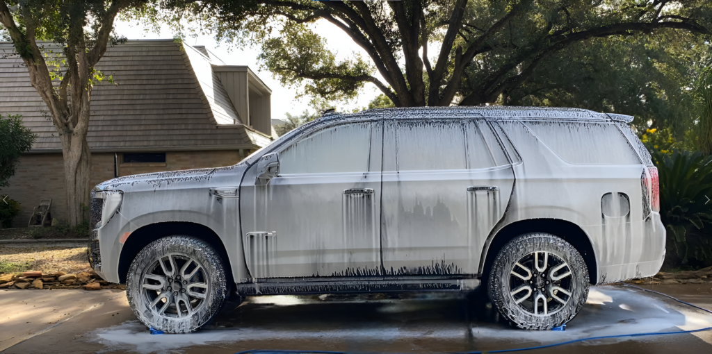 Close-up of a GMC Yukon covered in premium wash and wax soap during an exterior auto detailing service, showcasing a thorough car cleaning process for a polished, protected finish.